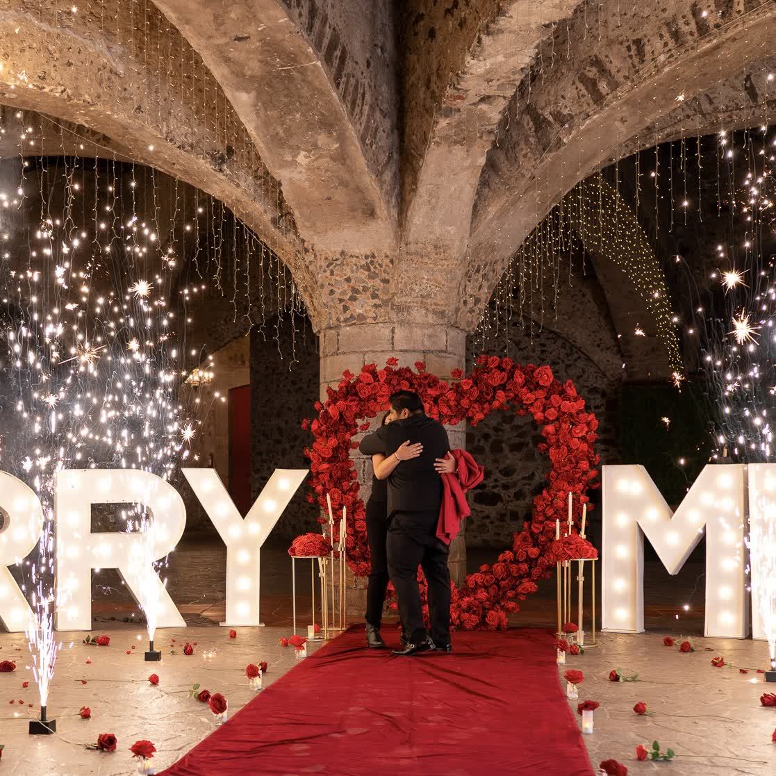 Pedida de matrimonio MARRY ME con corazón de rosas rojas y fuegos artificiales bajo bóveda de cantera