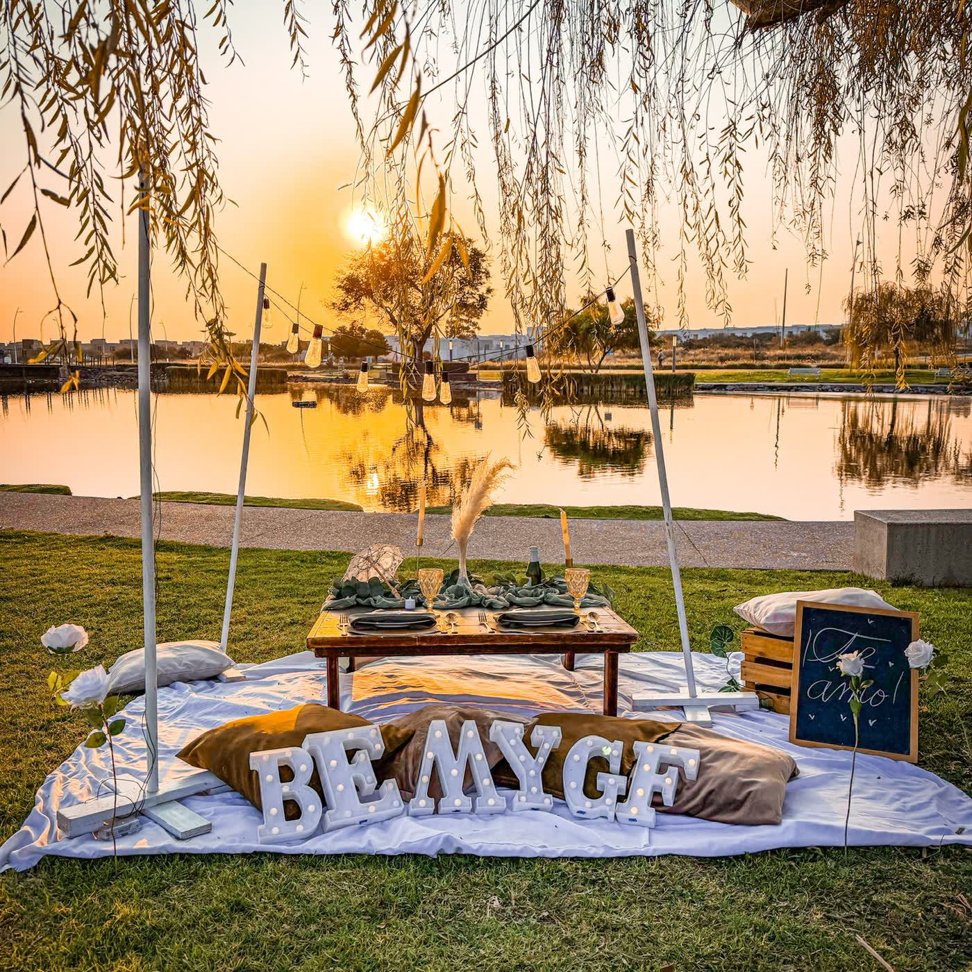 Picnic teepee con letras BE MY GF junto al lago al atardecer